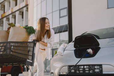 Elektrikli benzin istasyonunda kadın elektro arabayı şarj ediyor.