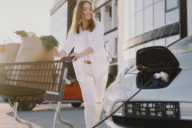 Elektrikli benzin istasyonunda kadın elektro arabayı şarj ediyor.