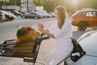 Elektrikli benzin istasyonunda kadın elektro arabayı şarj ediyor.