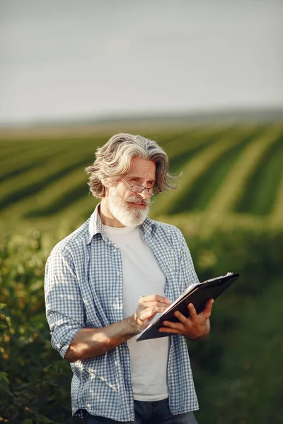 Antiguo granjero en camisa de pie en el campo con cuaderno —  Fotos de Stock