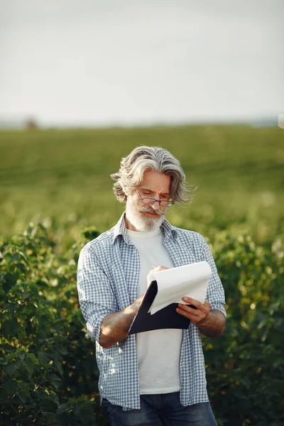 Antiguo granjero en camisa de pie en el campo con cuaderno —  Fotos de Stock