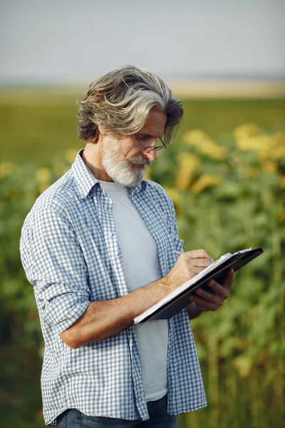 Antiguo granjero en camisa de pie en el campo con cuaderno —  Fotos de Stock