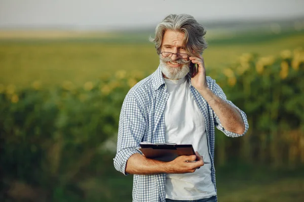 Старый фермер в рубашке, стоящий на поле с блокнотом — стоковое фото