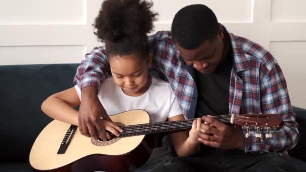Afro-Amerikaanse man die zijn dochtertje thuis gitaar leert spelen — Stockvideo