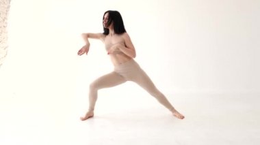 Bej kostümlü bir kadın beyaz arka planda dans ediyor.