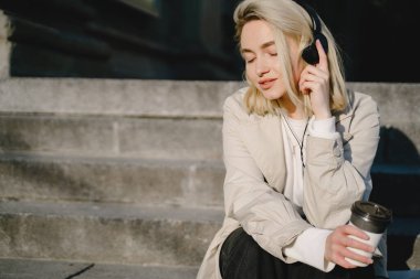 Merdivenlerde oturan kulaklıklı sarışın.