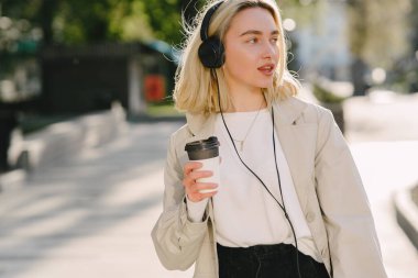 Sarışın yaz kentinde bir fincan kahveyle yürüyor.