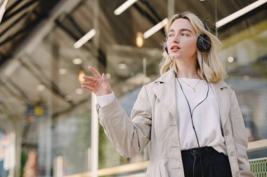 Sarışın, yaz şehrinde kulaklıklarla yürüyor.