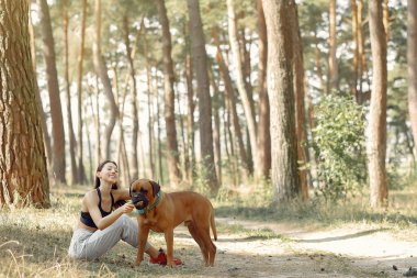 Ormanda oturan ve köpekle oynayan kız.
