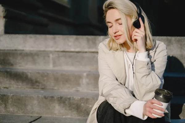 Blonde with headphones sitting on a stairs — Stock Photo, Image