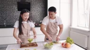 Evdeki mutfakta birlikte yemek pişiren mutlu Asyalı genç çiftin portresi.