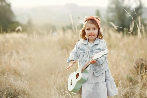 Zitieren Sie ein kleines Mädchen in einem Herbstpark, das auf einer Gitarre spielt — Stockfoto