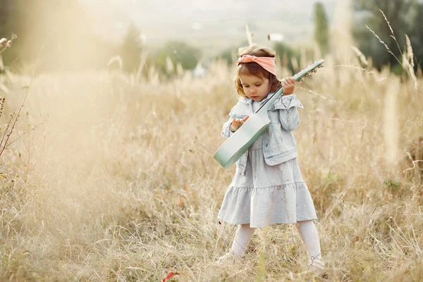 Zitieren Sie ein kleines Mädchen in einem Herbstpark, das auf einer Gitarre spielt — Stockfoto