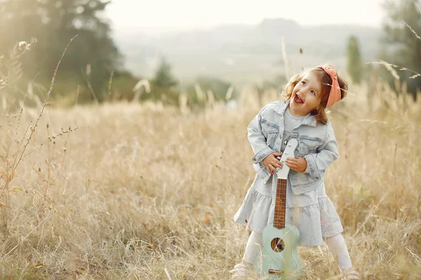 Zitieren Sie ein kleines Mädchen in einem Herbstpark, das auf einer Gitarre spielt — Stockfoto