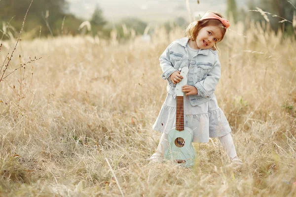 Zitieren Sie ein kleines Mädchen in einem Herbstpark, das auf einer Gitarre spielt — Stockfoto