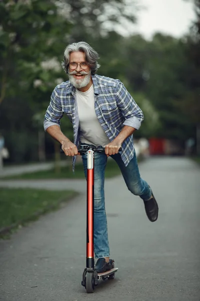 Portrait of elderly man with kick scooter in a summer park — Stock Photo, Image