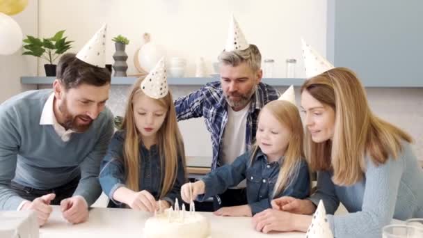 Батьки дивляться на дівчат, які кладуть свічки на торт на день народження — стокове відео