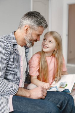 Modern olgun bir adam torunuyla birlikte yatak odasında kitap okuyor.