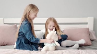 Yatakta yastıklarla oynayan iki küçük kız kardeş.