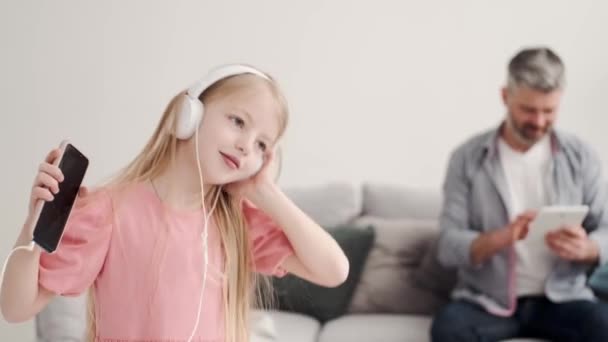Dziewczynka słuchająca muzyki w słuchawkach z dziadkiem — Wideo stockowe