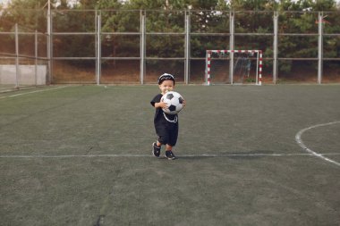 Küçük çocuk spor sahasında futbol oynuyor.