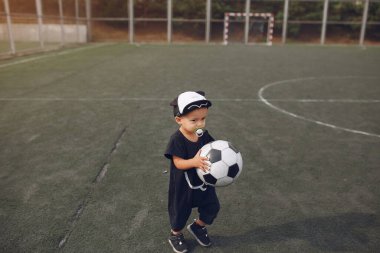 Küçük çocuk spor sahasında futbol oynuyor.