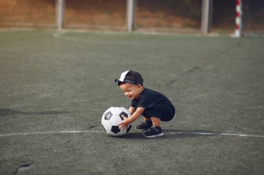 Küçük çocuk spor sahasında futbol oynuyor.