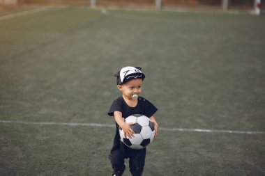 Küçük çocuk spor sahasında futbol oynuyor.