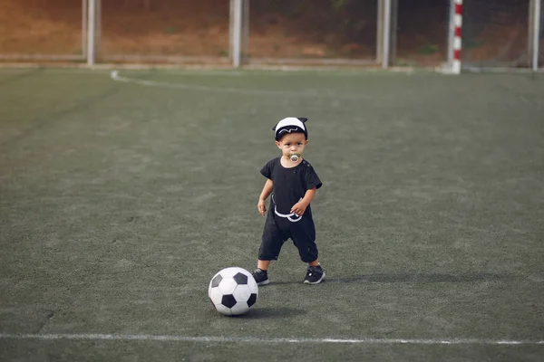 Küçük çocuk spor sahasında futbol oynuyor.