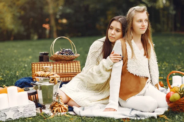 Элегантные и стильные девушки сидят в осеннем парке — стоковое фото