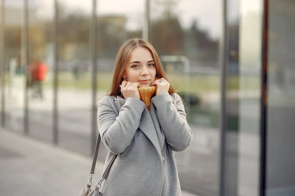 Dívka stojící u velké budovy v šedém kabátě — Stock fotografie