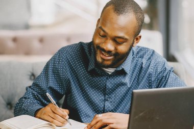 Dizüstü bilgisayarın arkasında çalışan bir adam deftere, kafeye yazı yazıyor.