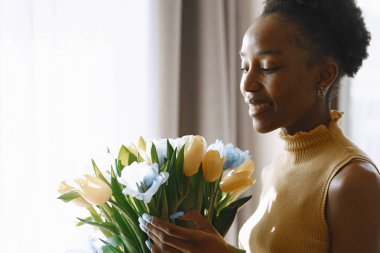 Pencere kenarında çiçek demeti olan Afrikalı bir kız.