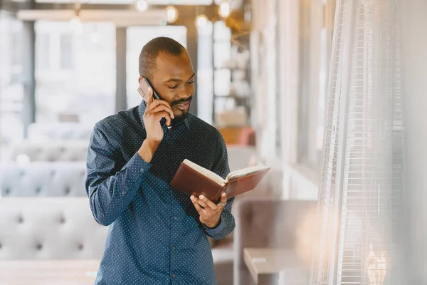 Homem sentado em um café e falando ao telefone, segurando um caderno. — Fotografia de Stock