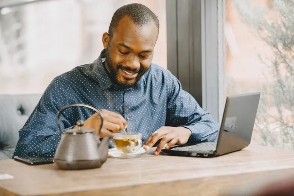 Homem sentado em um café e trabalhando atrás de um laptop, escrevendo em um caderno e beber um chá. — Fotografia de Stock