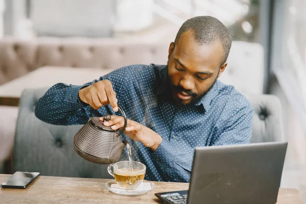 Homem sentado em um café e trabalhando atrás de um laptop e derramando um chá em uma xícara. — Fotografia de Stock
