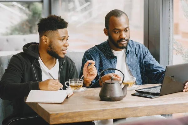 Dois homens sentados em um café e trabalhando atrás de um laptop e beber um chá. — Fotografia de Stock