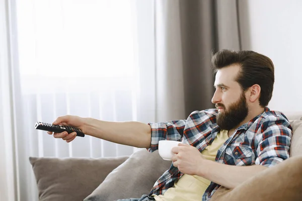 Hombre bebiendo café y viendo televisión en el sofá — Foto de Stock