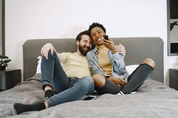 Yatakta birlikte televizyon izleyen çok ırklı bir çift. — Stok fotoğraf