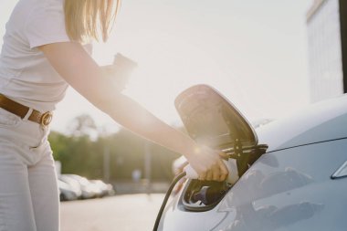 Elektrikli benzin istasyonunda kadın elektro arabayı şarj ediyor.
