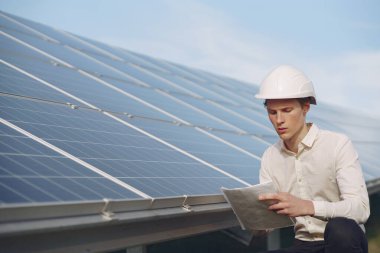 Güneş bataryasının yanında beyaz kasklı bir iş adamı.