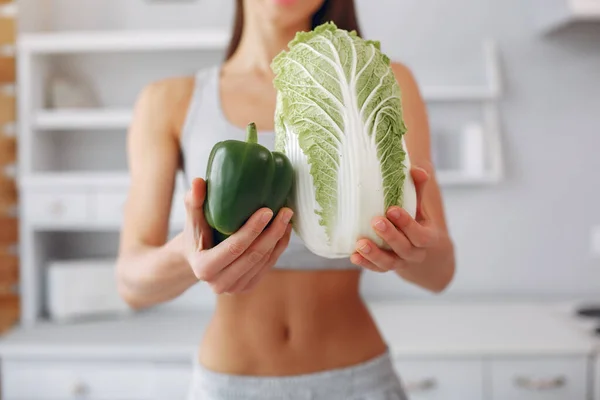 Menina bonita e desportiva em uma cozinha com um legumes — Fotografia de Stock