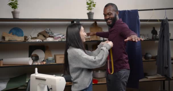 Coreano alfaiate feminino medindo homem negro na oficina — Vídeo de Stock