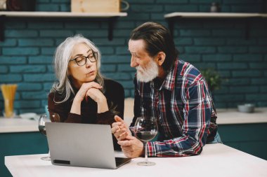 Mutfakta dizüstü bilgisayar kullanan mutlu yaşlı çift.