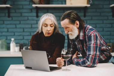 Mutfakta dizüstü bilgisayar kullanan mutlu yaşlı çift.