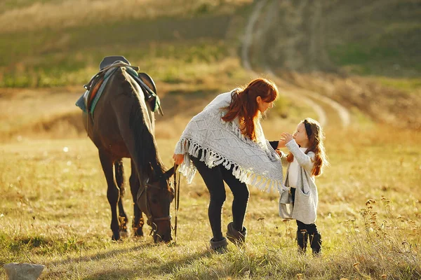 Mother and daughter in a field playing with a horse — Stock Photo, Image