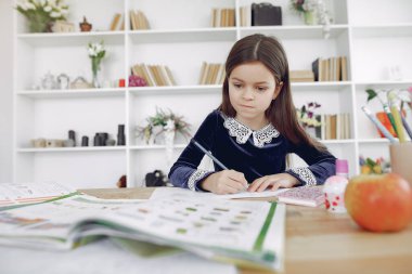 Kitaplarla dolu bir masada oturan küçük kız.