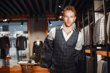 Sakallı yakışıklı bir adam dükkanda ceket seçiyor.