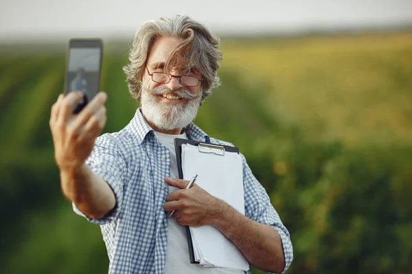 Antiguo granjero en camisa de pie en el campo con cuaderno —  Fotos de Stock