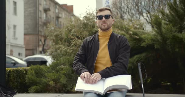 Jonge slechtziende man zittend op een bankje in het stadspark — Stockvideo